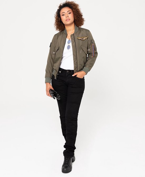Model in een groene pilotenjas, witte top, zwarte jeans en zwarte laarzen.