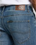 Close-up van de achterkant van een spijkerbroek met een bruine Lee-patch en een klein Lee-logo op de achterzak.