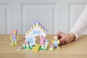 Hand met PLUS PLUS blokjes bouwt een huisje met twee figuurtjes en een regenboog.