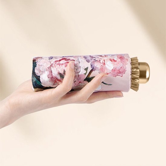 Hand houdt een compacte, gesloten paraplu met roze pioenrozen schilderij, gouden uiteinde.