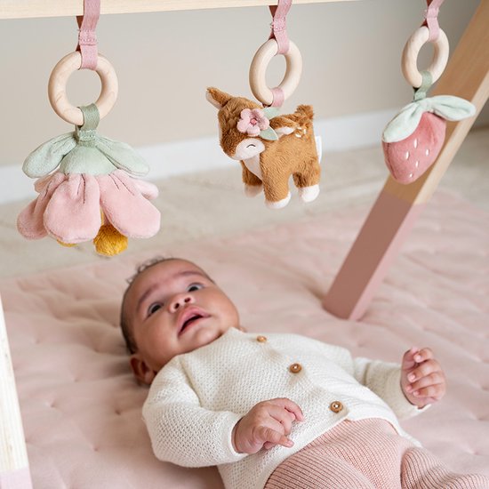 Baby ligt onder houten babygym met speeltjes: bloem, hertje en aardbei.