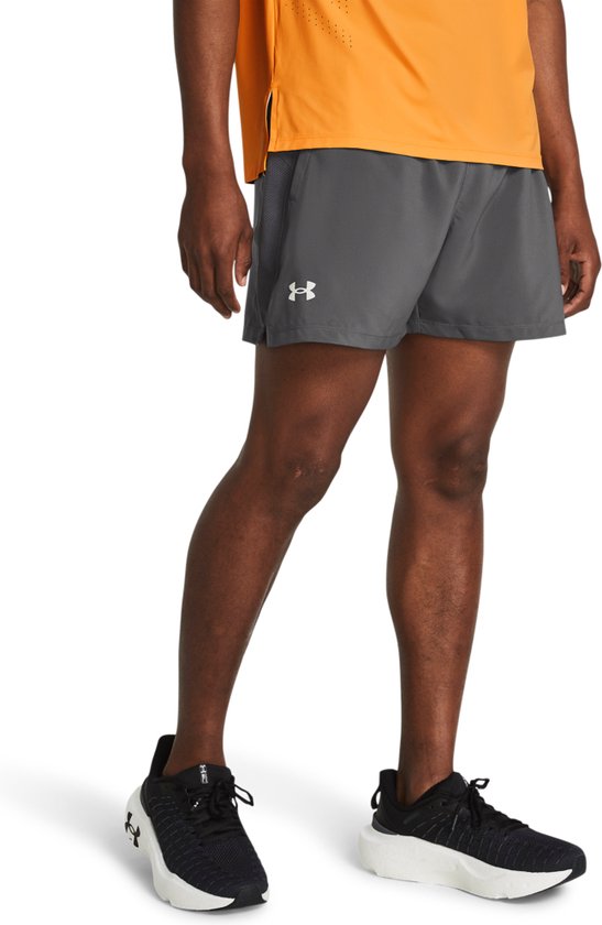Model met grijze Under Armour sportshort, mesh panelen aan de zijkant en wit logo, gecombineerd met oranje shirt.