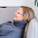 Vrouw met rode lichtbril ontspannen op een grijze bank.