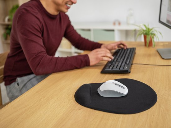 Souris blanche sur un tapis de souris XL noir avec repose-poignet. Un homme porte un pull bordeaux et tape sur un clavier.