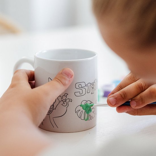 Kind schildert met een penseel groen op een witte mok met Stitch-tekening.