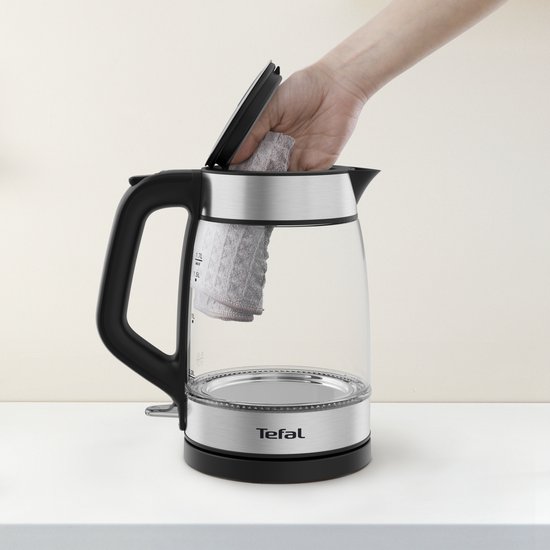 Hand reinigt glazen waterkoker met een doekje, zilverkleurige en zwarte details.