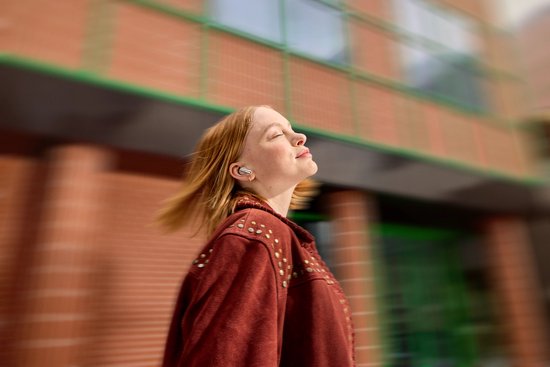 Vrouw met gesloten ogen, genietend van muziek met paarse JBL Live Beam 3 oordopjes.