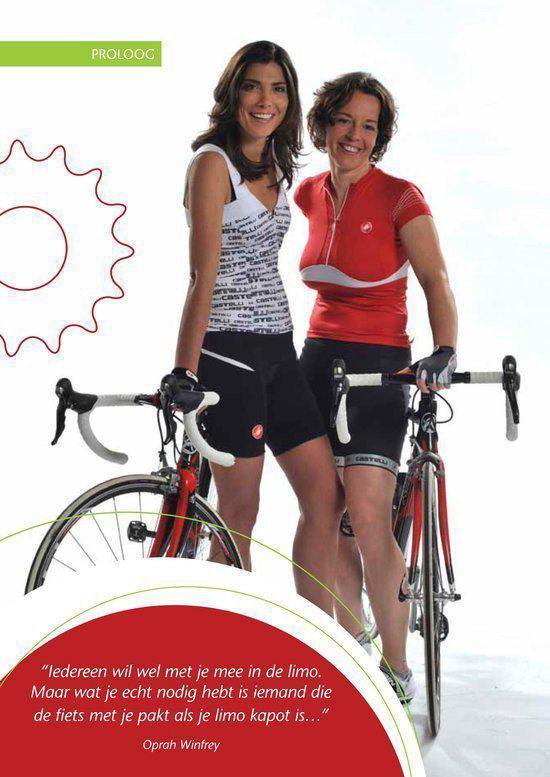 Twee lachende vrouwen in fietskleding, staand naast hun racefietsen.