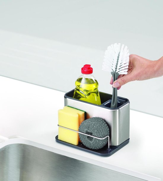 Une main saisit une brosse verte d'un organisateur d'évier en acier inoxydable avec éponge et savon.