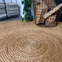Rond jute vloerkleed met spiraalpatroon in de woonkamer, met houtmand ernaast.