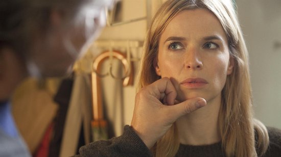 Een blonde vrouw met lange haren, die haar kin vasthoudt en peinzend wegkijkt.