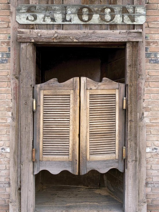 Portes doubles en bois à persiennes sous un panneau 'SALOON', sur un mur de briques.