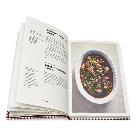 Stoofpot van varkensvlees met doperwten in een witte schaal op een boekpagina.