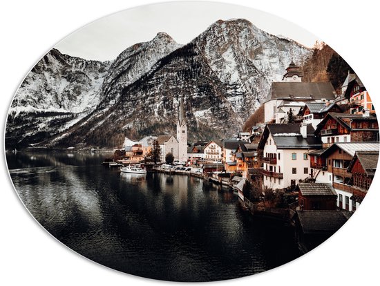WallClassics - PVC Schuimplaat Ovaal - Klein Dorpje tussen Bergen bij Water - 108x81 cm Foto op Ovaal  (Met Ophangsysteem)