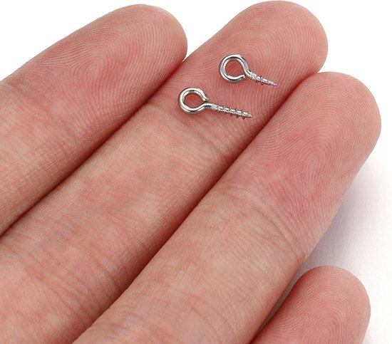 Twee zilverkleurige oogschroeven met schroefdraad op een vingernagel.