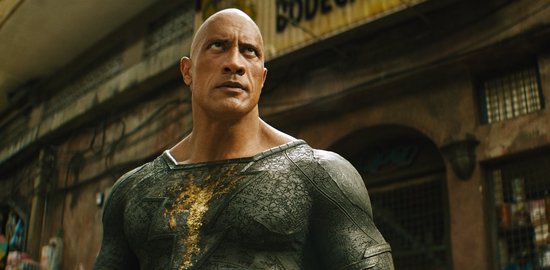 Dwayne Johnson als Black Adam, gekleed in een grijs kostuum met een gouden bliksemschicht op de borst.