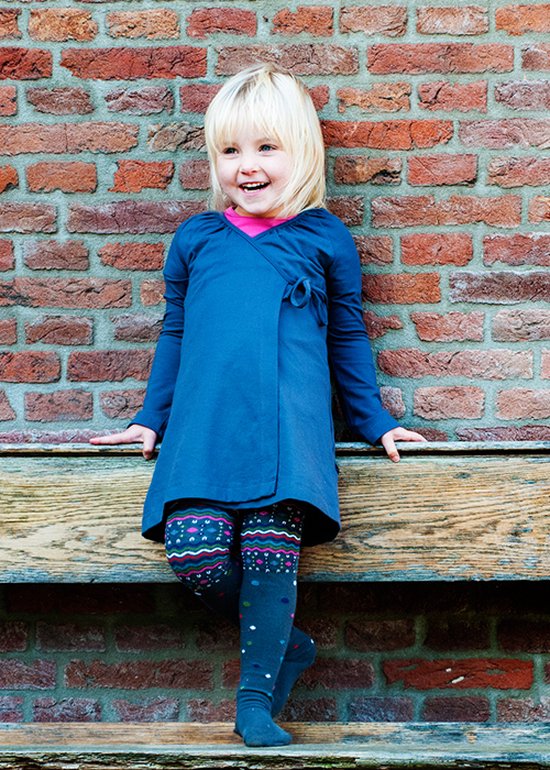 Meisje met blond haar in blauwe wikkeljurk, patroonmaillot met zigzaggend patroon en sokken.