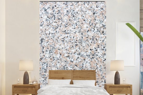 Muur met granietprint boven een tweepersoonsbed met houten hoofdeinde.