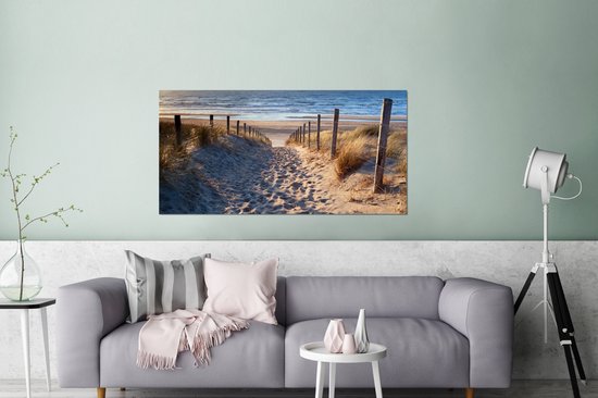 Un sentier à travers les dunes, bordé d'herbes, mène à la mer au coucher du soleil.