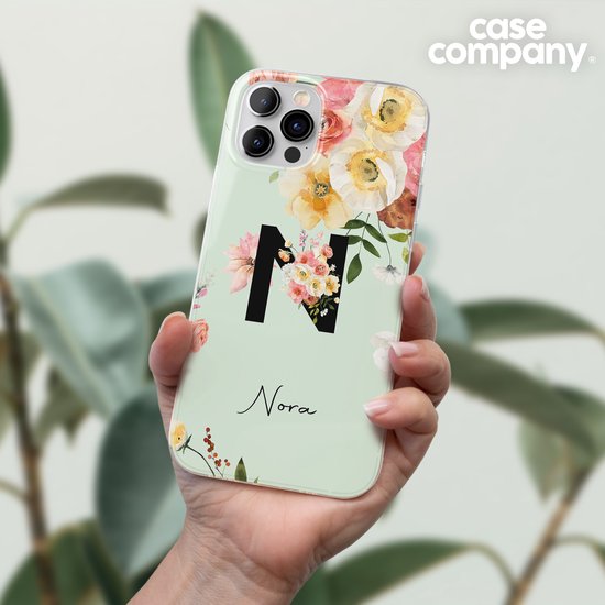 Hand houdt lichtgroen telefoonhoesje vast met zwart initiaal 'N', omringd door roze en gele bloemen, en de tekst 'Nora'.