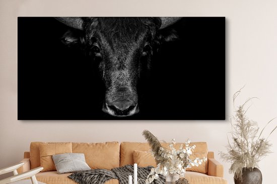 Toile noir et blanc de la tête d'un taureau sur fond sombre, au-dessus d'un canapé orange.