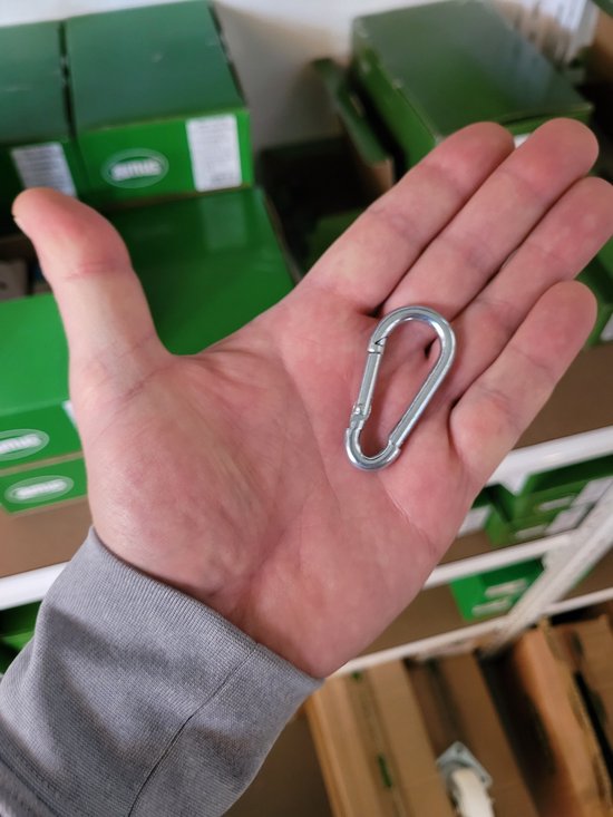 Hand met zilverkleurige karabijnhaak in de palm. Groene dozen op de achtergrond.
