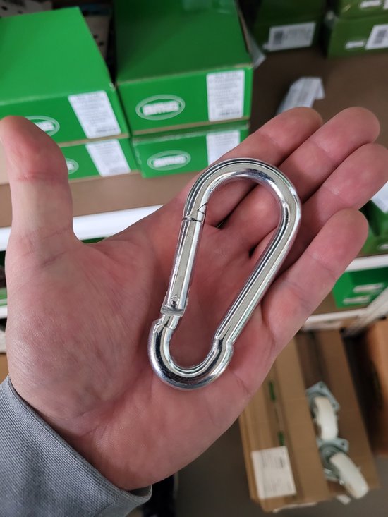 Hand die een zilverkleurige karabijnhaak van metaal met veersluiting vasthoudt.