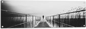 WallClassics - Tuinposter – Persoon op Brug bij het Water in het zwart-wit - 120x40 cm Foto op Tuinposter  (wanddecoratie voor buiten en binnen)