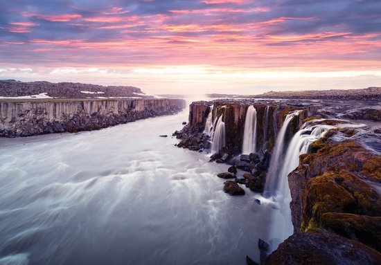 Une large cascade dévale des falaises rocheuses sous un ciel de coucher de soleil rose et violet.