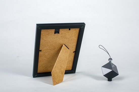 Zwarte fotolijst, achterkant met standaard en ophangoog. Naast de lijst een decoratief zwart object.