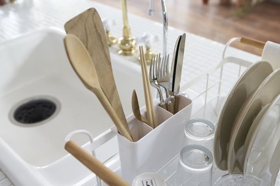 Gros plan d'ustensiles de cuisine en bois et en métal dans un égouttoir blanc à côté d'un évier.
