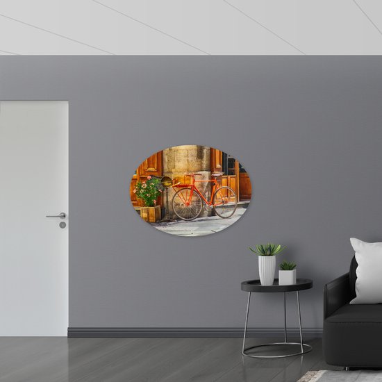 WallClassics - Plaque ovale en mousse PVC - Vélo Oranje dans un bâtiment en pierre - 108x81 cm Photo sur ovale (avec système de suspension)