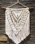Groot macramé wandkleed met gedetailleerd geometrisch en botanisch patroon, hangend aan een boomtak.