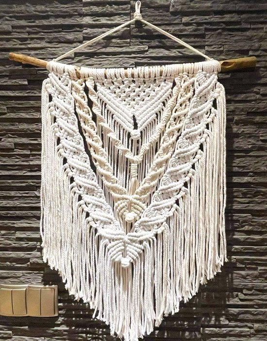 Groot macramé wandkleed met gedetailleerd geometrisch en botanisch patroon, hangend aan een boomtak.