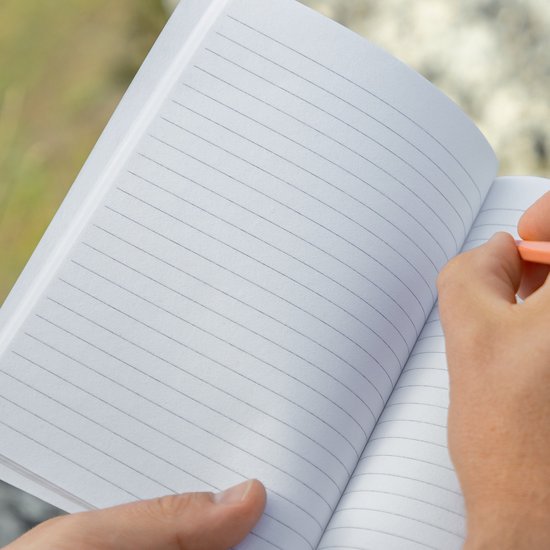 Carnet ouvert gris ligné, tenu par une personne avec un crayon orange.