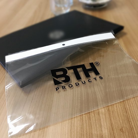 Een doorzichtige plastic zak met een zwart logo "BTH PRODUCTS" erop, liggend op een laptop op een houten tafel.