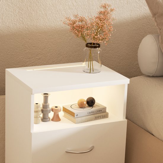 Wit nachtkastje met open vak, verlichting, decoratie, boeken en een lade.