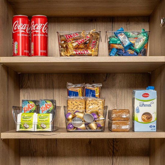Een open keukenkast met georganiseerde producten op houten planken. Bakken met frisdrank, snoep, thee, koffiecups en ontbijtgranen.