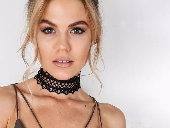 Close-up van een model met blonde haren die een zwarte, kanten choker met opengewerkt patroon draagt.