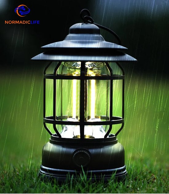 Lanterne de camping noire avec cadre en métal, lumière LED allumée, sur l'herbe sous la pluie.