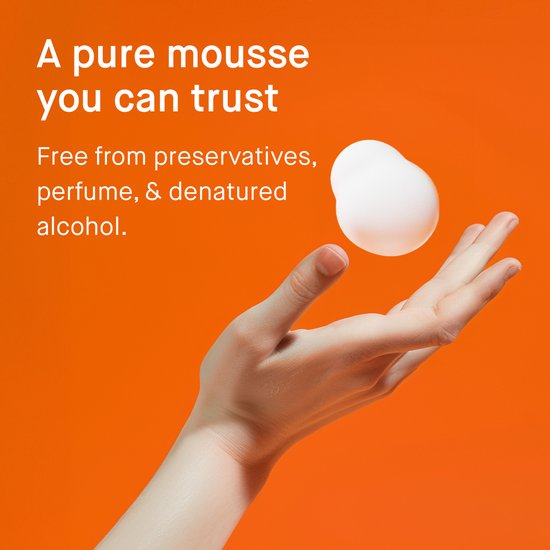 Hand met witte mousse en een abstracte witte vorm op oranje achtergrond.
