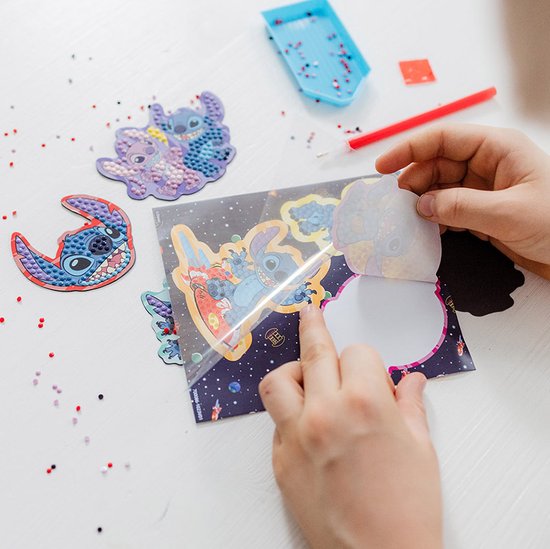 Un enfant colle un autocollant sur un magnet Stitch diamond painting. Le magnet se déroule dans l'espace, avec Stitch surfant sur une planche.