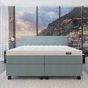 Lichtblauwe boxspring met matras op een grijs tapijt, met uitzicht op een kuststad.
