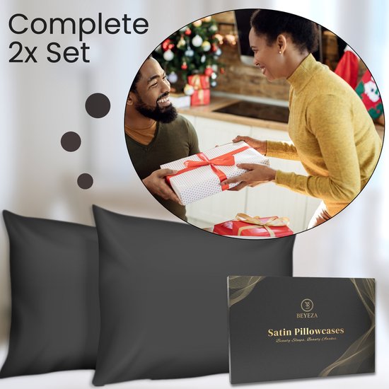 Een man overhandigt een cadeau aan een lachende vrouw, met op de voorgrond twee zwarte satijnen kussenslopen.