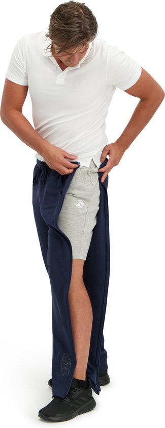 Jongen met donkerblauwe joggingbroek met ritsen, die een grijze korte broek draagt.