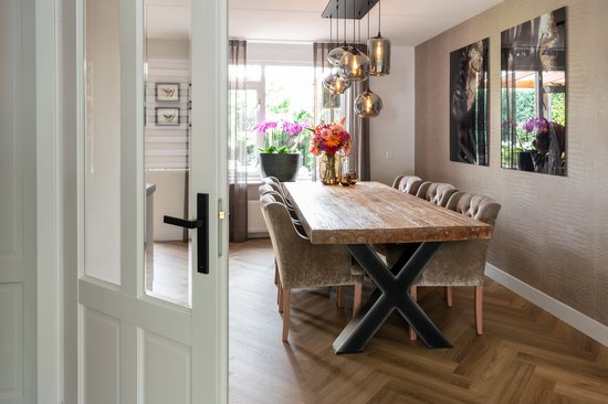 Eetkamer met grote houten tafel, gestoffeerde stoelen en design hanglampen.