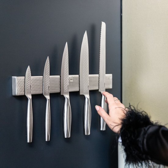 Vrouw pakt een van de vijf zilverkleurige RVS messen van een magneetstrip.