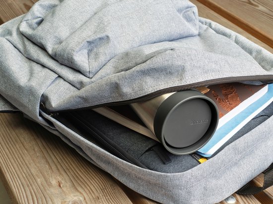 Roestvrijstalen thermosbeker met grijs deksel in een open grijze rugzak tussen boeken.