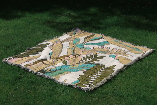 Uitgevouwen beige deken met botanische print op groen gras.