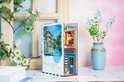 Houten boekensteun met straatafbeelding en miniatuur café, met bloemen op de achtergrond.